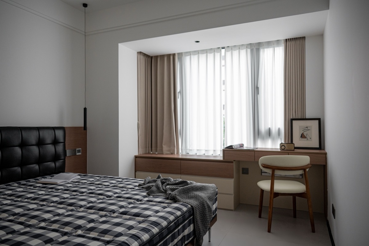 Chambre moderne aux tons neutres avec un lit, un bureau et une chaise devant une fenêtre voilée