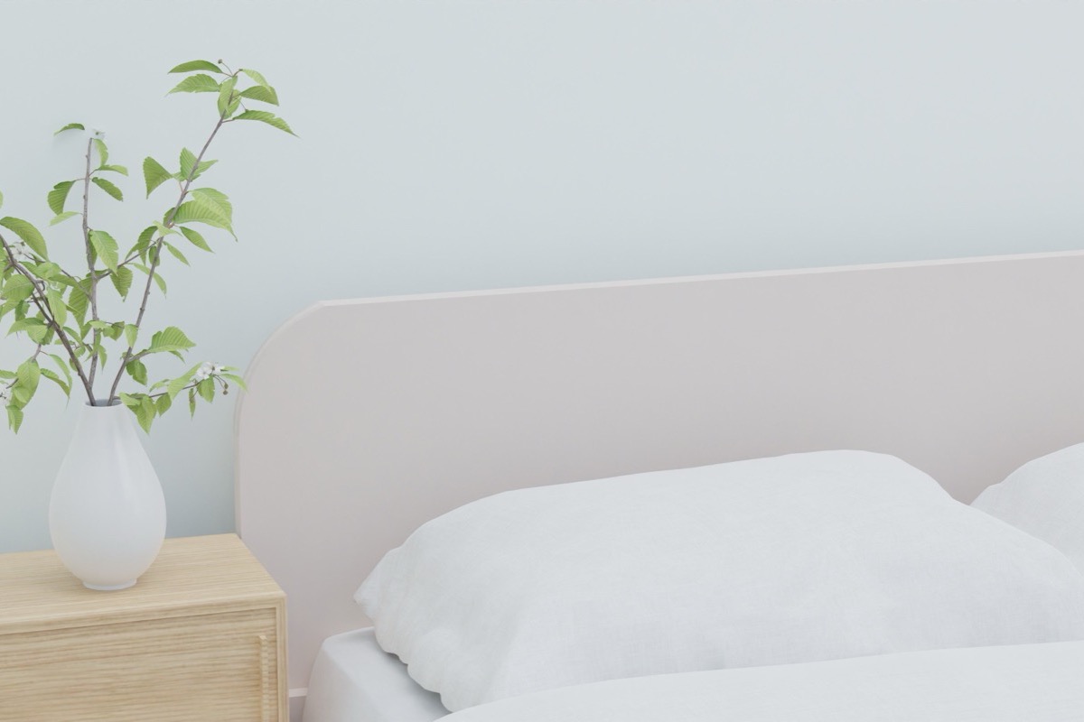 Tête de lit claire, linge de lit blanc et branche verte dans un vase sur une table de chevet en bois
