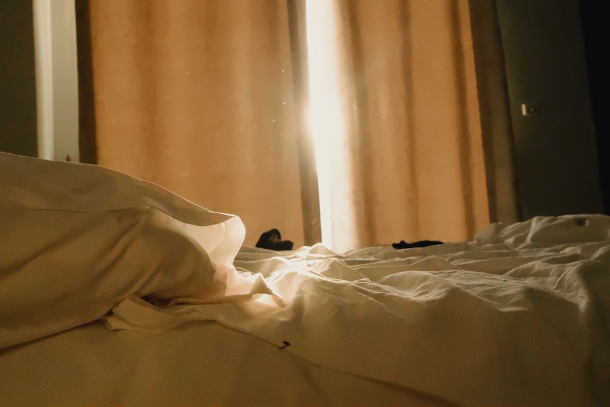Lit défait dans une chambre où la lumière du matin filtre entre les rideaux
