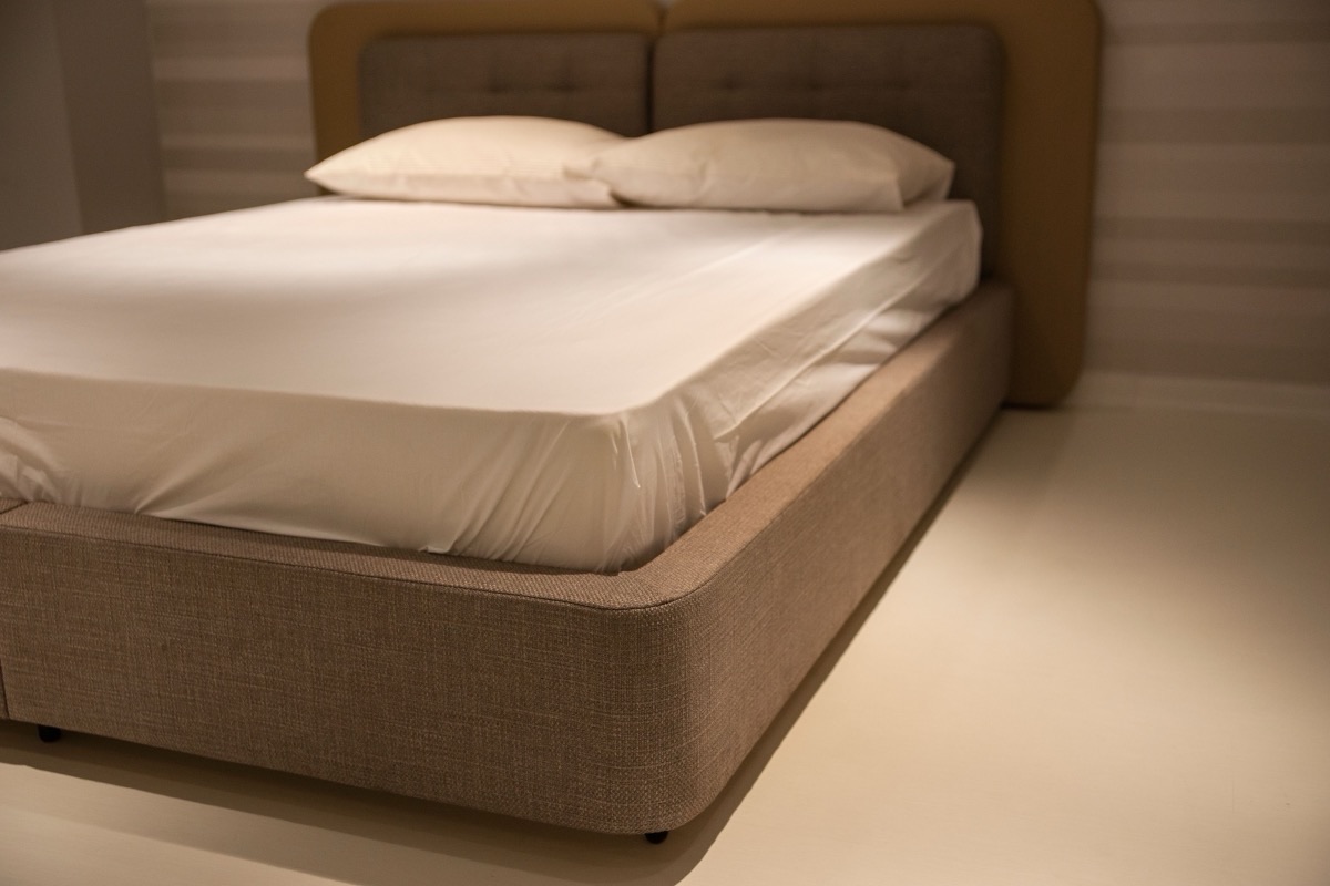 Matelas recouvert d'un drap tendu sur un cadre de lit clair, dans une chambre sobre