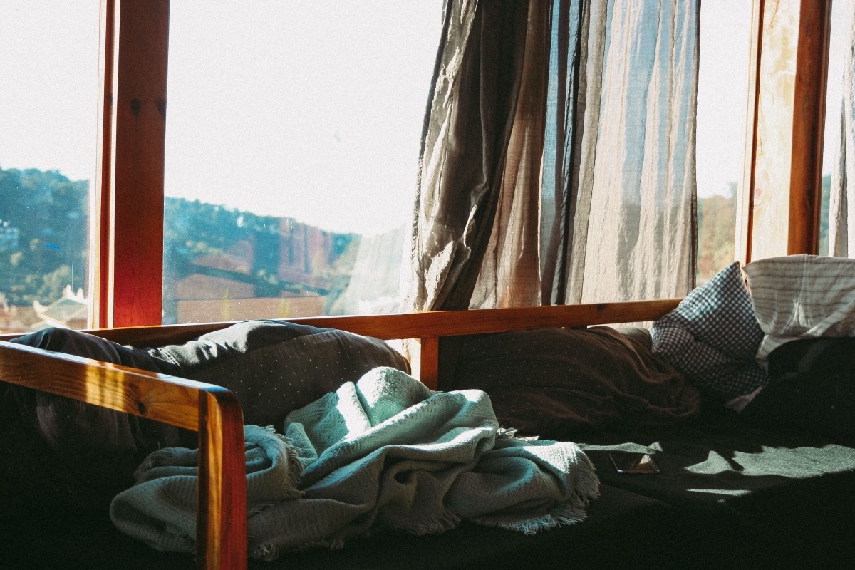 Lumière naturelle du matin entrant largement par une fenêtre à rideaux et éclairant un lit défait