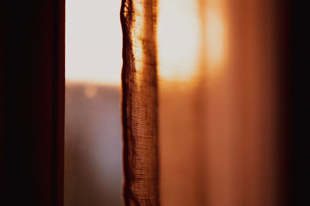 Lumière chaude du petit matin filtrant par un rideau tiré devant une fenêtre