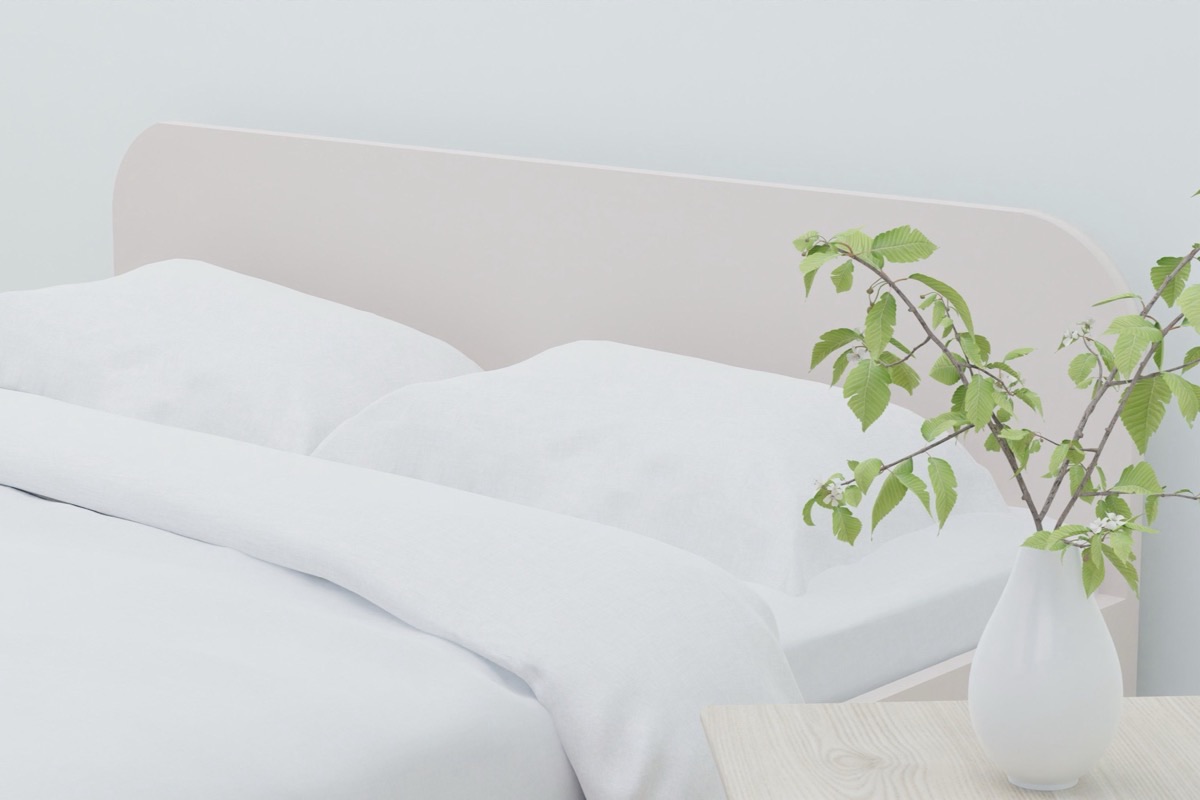 Lit aux draps blancs légers dans une chambre claire et aérée, avec une branche verte dans un vase