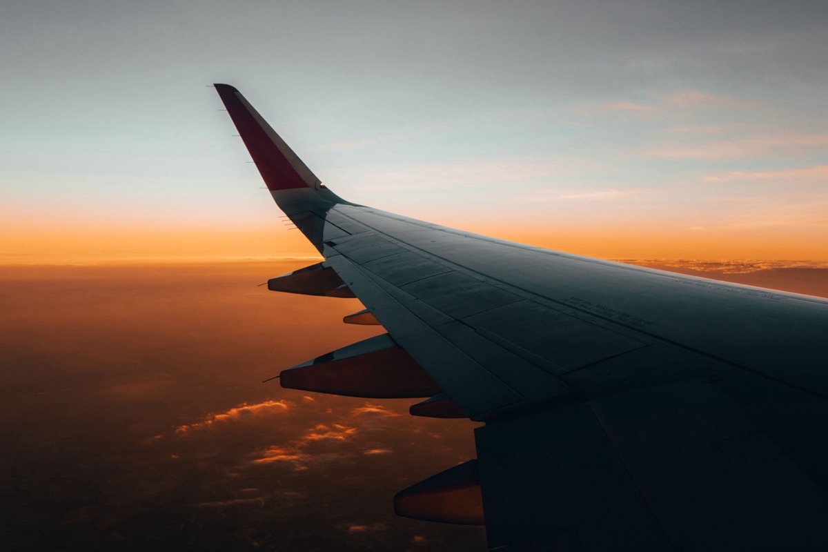 Aile d'avion survolant les nuages au lever du jour, ciel orangé à l'horizon