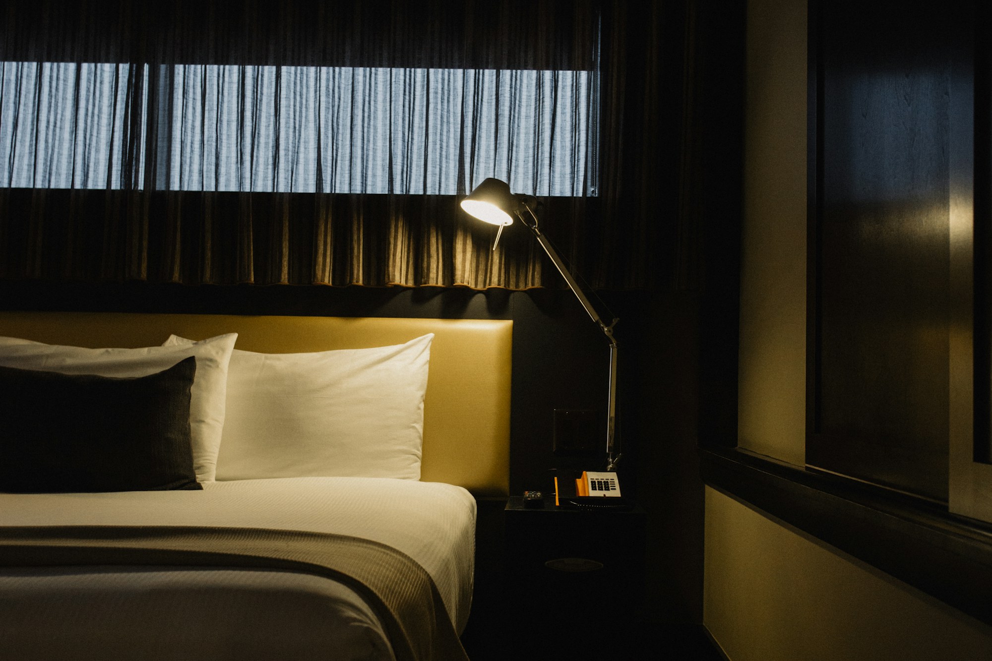 Chambre a coucher dans la penombre, lit et lampe de chevet allumee le soir